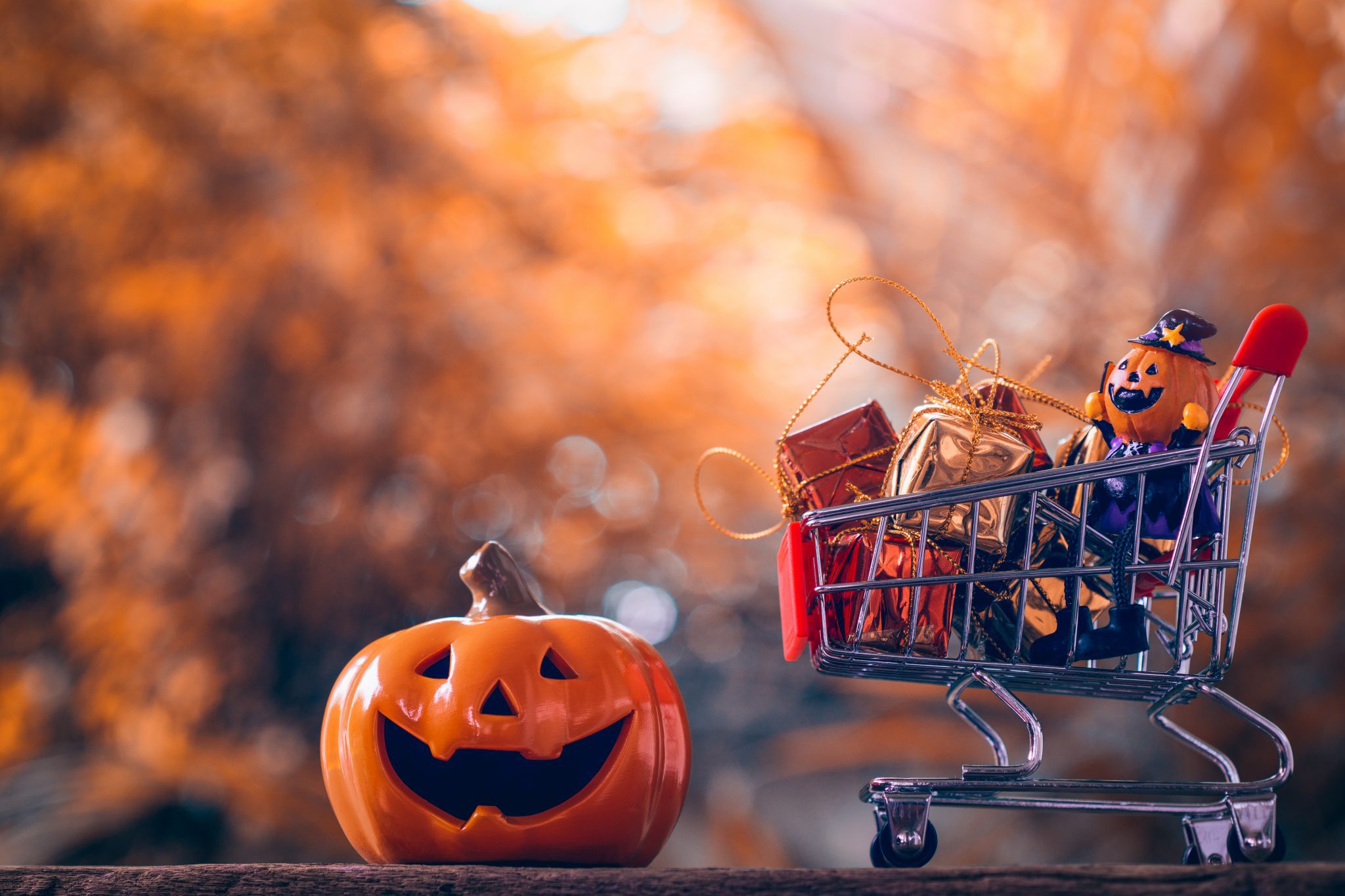 Halloween pumpkins with shopping cart on wood background.